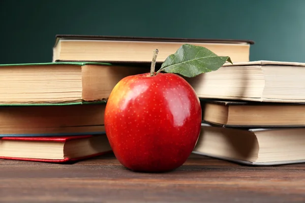 School books with apple on blackboard background