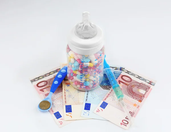 Feeding bottle full of pills with syringe, spoon and euro banknotes on white background