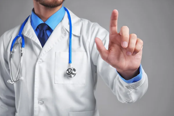 Male doctor pointing on grey background