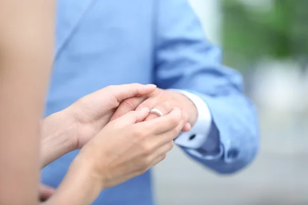 Bride putting ring on groom finger outdoor