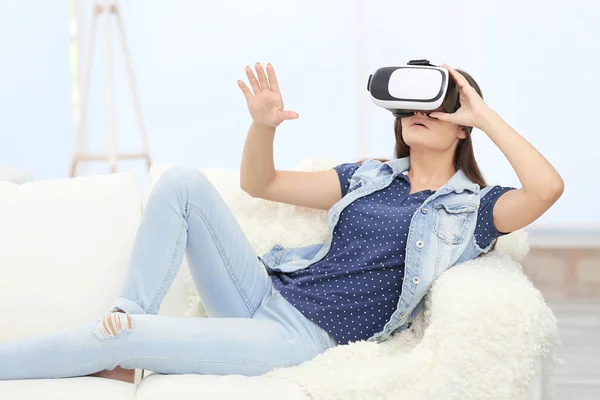 Young woman wearing virtual reality glasses on sofa in a room