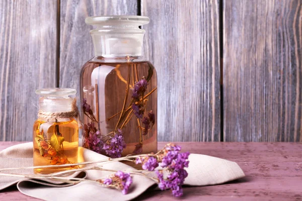 Bottles of herbal tincture and brunch of flowers on a napkin on a wooden table in front of wooden wall