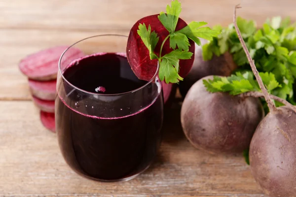 Glass of fresh beet juice and vegetables on wooden background