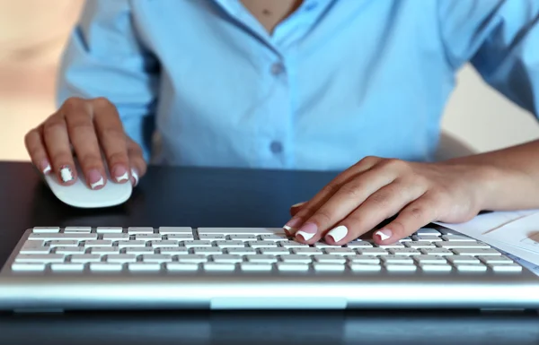 Female hands typing on keyboard, close-up, on dark background