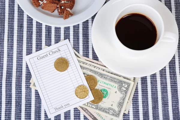 Check, cup of coffee and money on table close-up