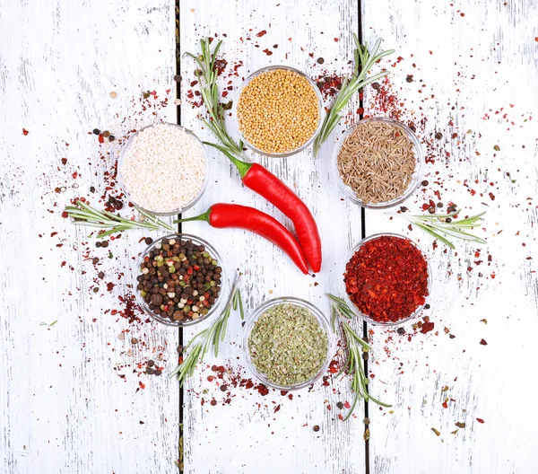 Spices in glass round bowls with herbs and chilly pepper on wooden background