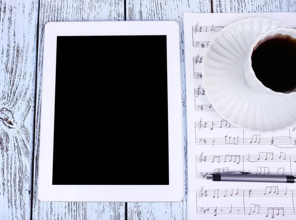 Tablet, cup of coffee printed music and earphones on wooden background