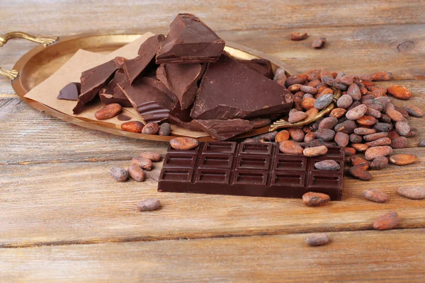 Cracked chocolate bar and cocoa beans on wooden background