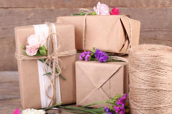 Beautiful gifts with flowers and decorative rope, on old wooden background
