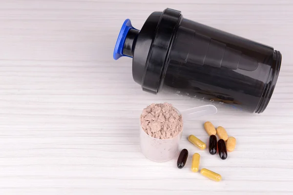 Whey protein powder in scoop with vitamins and plastic shaker on wooden background
