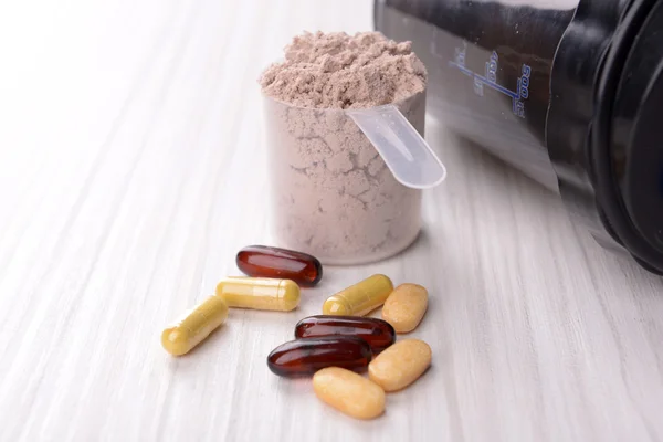 Whey protein powder in scoop with vitamins and plastic shaker on wooden background