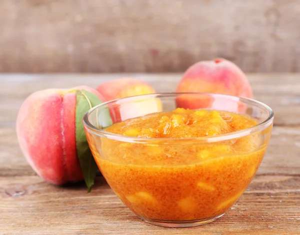 Tasty peach jam with fresh peaches on wooden table