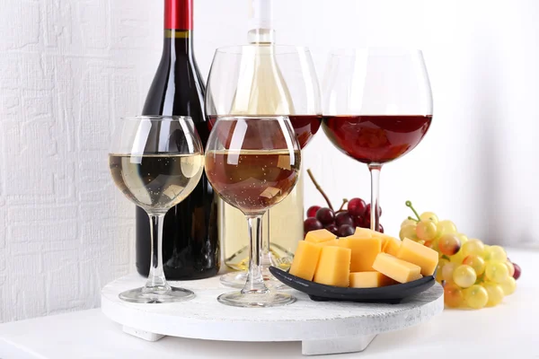 Bottles and glasses of wine, cheese and ripe grapes on table in room