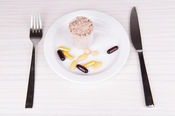 Whey protein powder in scoop with vitamins on plate on wooden background