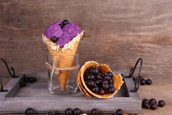 Tasty ice cream with berries in waffle cone on brown wooden background