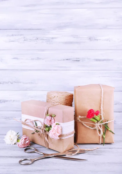 Beautiful gifts with flowers and decorative rope, on old wooden background