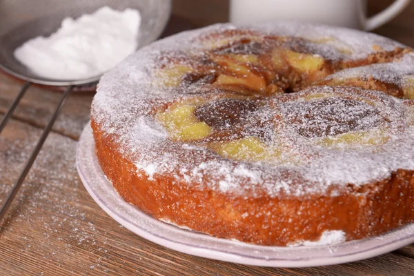 Delicious cake and sieve with powdered sugar on wooden table