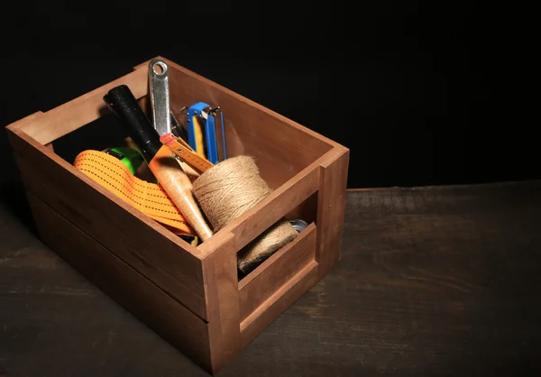 Wooden box with different tools, on wooden table, on dark background
