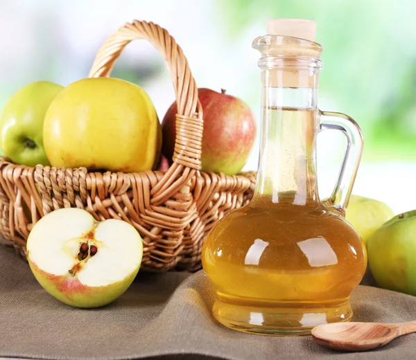 Apple cider vinegar in glass bottle and ripe fresh apples, on wooden table, on nature background