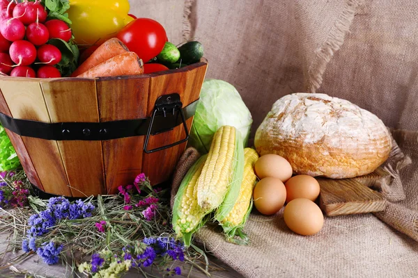 Big round wooden basket with vegetables, milk and bread on sacking background