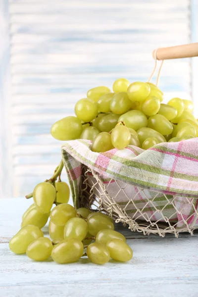 Ripe grapes in metal basket with napkin on wooden table on light background