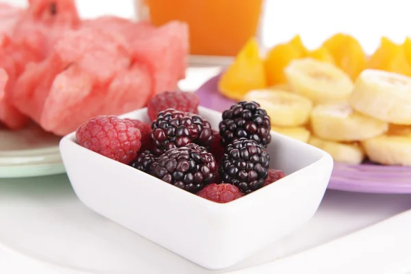 Slices of fruits with berries on plate and glass of juice close up