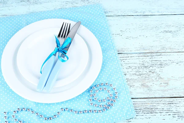 White plates, fork, knife and Christmas decoration on blue polka dot napkin on wooden background