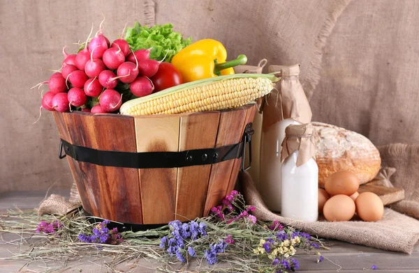 Big round wooden basket with vegetables, milk and bread on sacking background