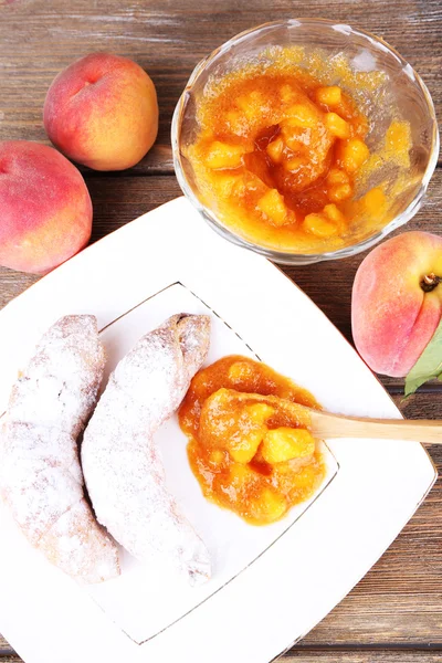 Tasty peach jam with fresh peaches and croissants on wooden table