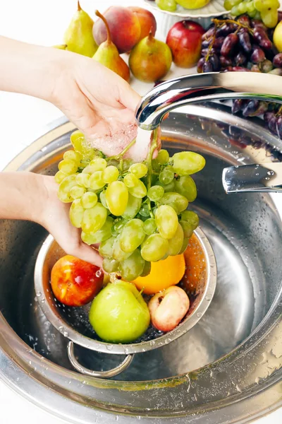Woman\'s hands washing grapes and other fruits in colander in sink