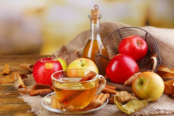 Composition of  apple cider with cinnamon sticks, fresh apples and autumn leaves on wooden background