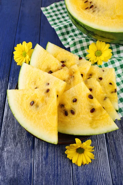 Slices of yellow watermelon on checkered napkin and yellow flowers on wooden background