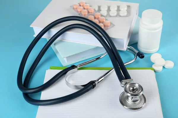 Medical stethoscope with books and tablet on blue background