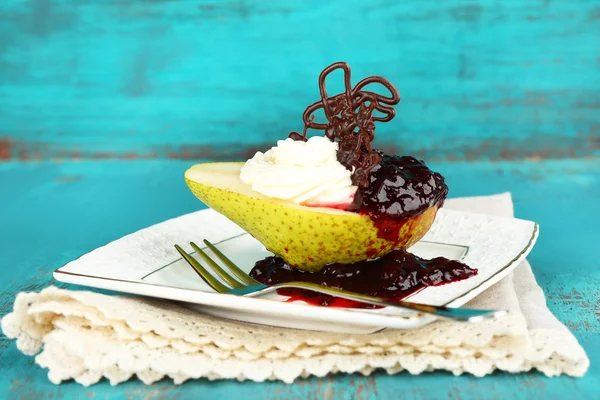 Tasty dessert with pear, cream and berry sauce on plate, on color wooden background