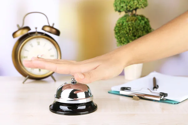 Female hand ring bell on  hotel reception desk, on bright background