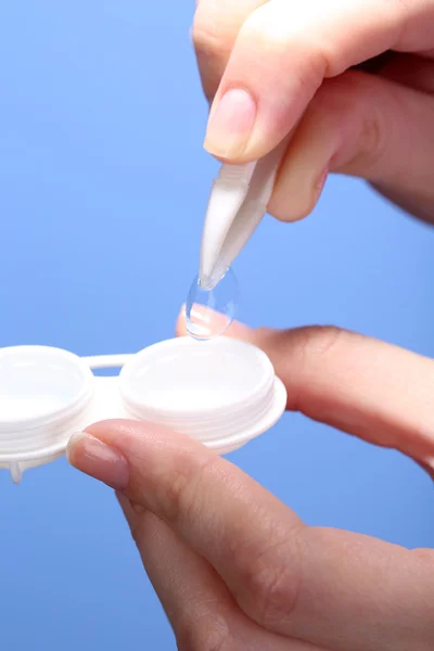 Woman holding container with contact lenses, close-up, on blue background