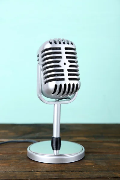 Old metal microphone on wooden table on light blue background