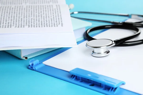 Medical stethoscope with books and folder on blue background