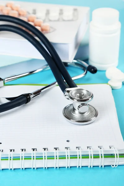 Medical stethoscope with books and tablet on blue background