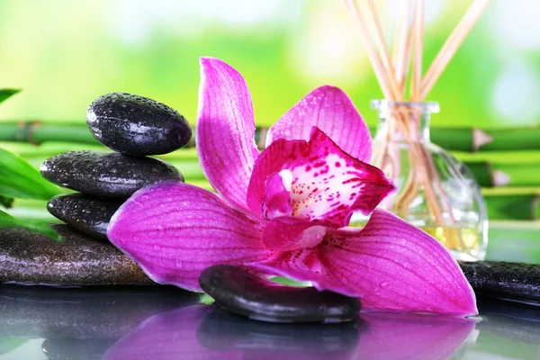 Spa stones, sticks, bamboo branches and lilac orchid on table on natural background