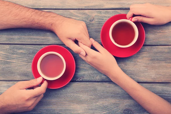 Tea cups and holding hands at the wooden table