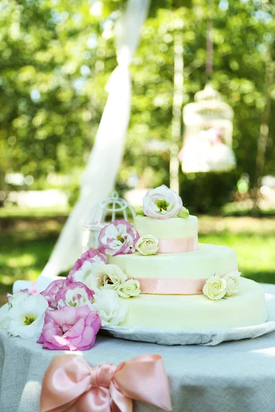 Beautiful wedding cake with flowers on table, outdoors