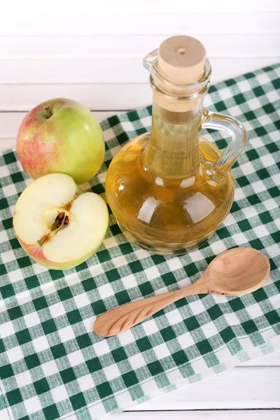 Apple cider vinegar in glass bottle and ripe fresh apples, on wooden table