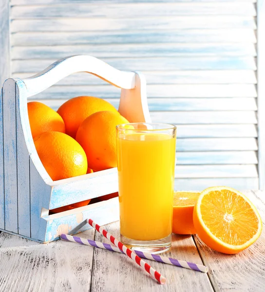 Glass of orange juice and fresh oranges in wooden box on wooden table on wooden wall background