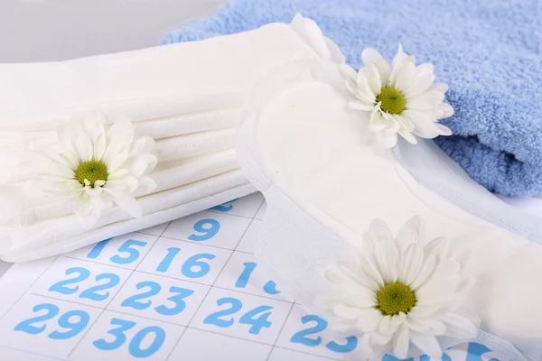 Sanitary pads, calendar, towel and white flowers on light background