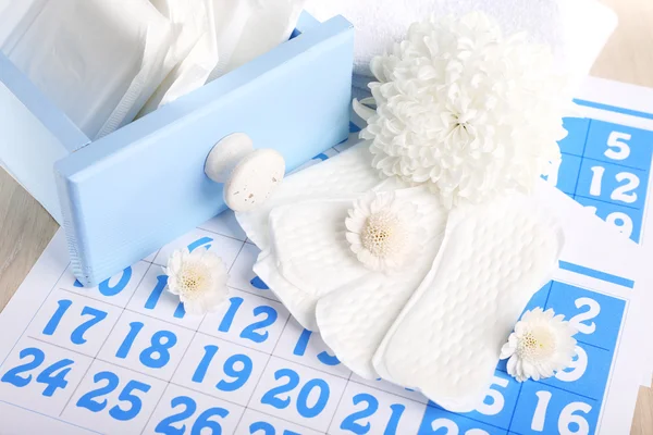 Sanitary pads in box and sanitary pads and white flowers on blue calendar on light grey background