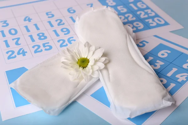 Sanitary pads, calendar and white flower on light blue background