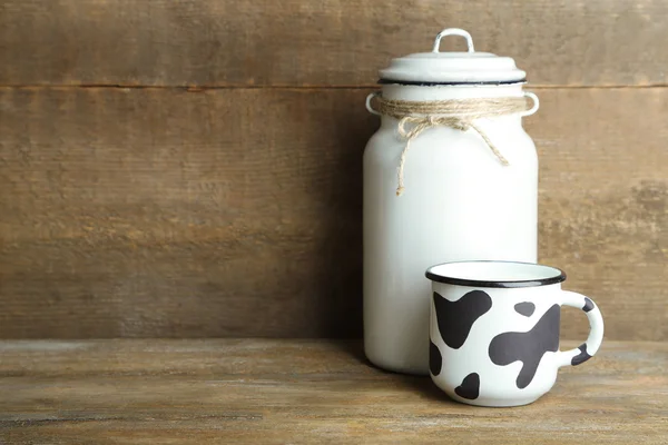 Retro can for milk and mug of milk on wooden table