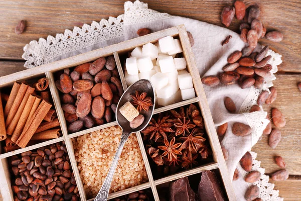 Wooden box with set of coffee and cocoa beans, sugar cubes, dark chocolate, cinnamon and anise, close-up, on wooden background