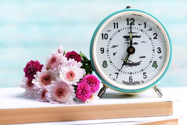Beautiful flowers with clock and book on table on light blue background